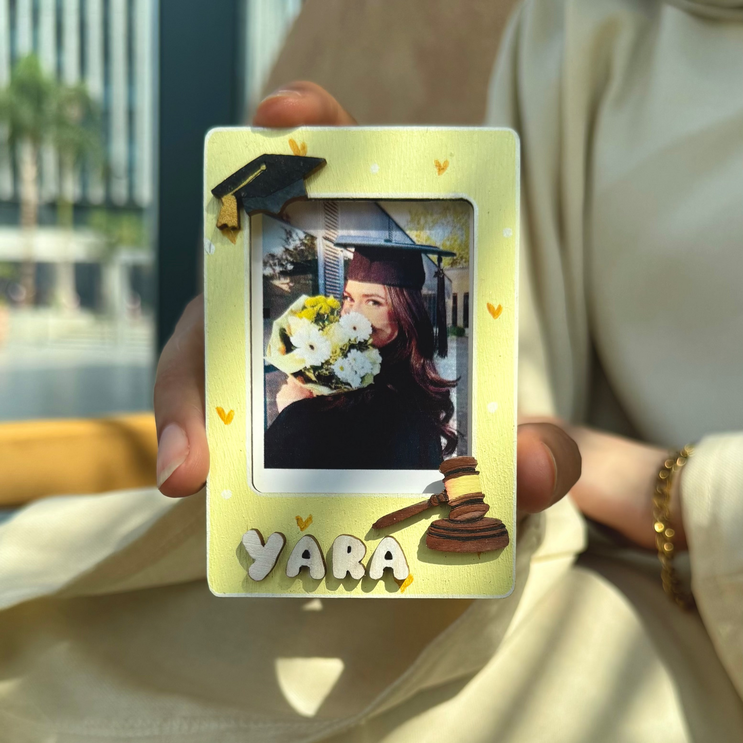 Graduation-themed photo frame with a picture of a graduate holding flowers, held by a person.