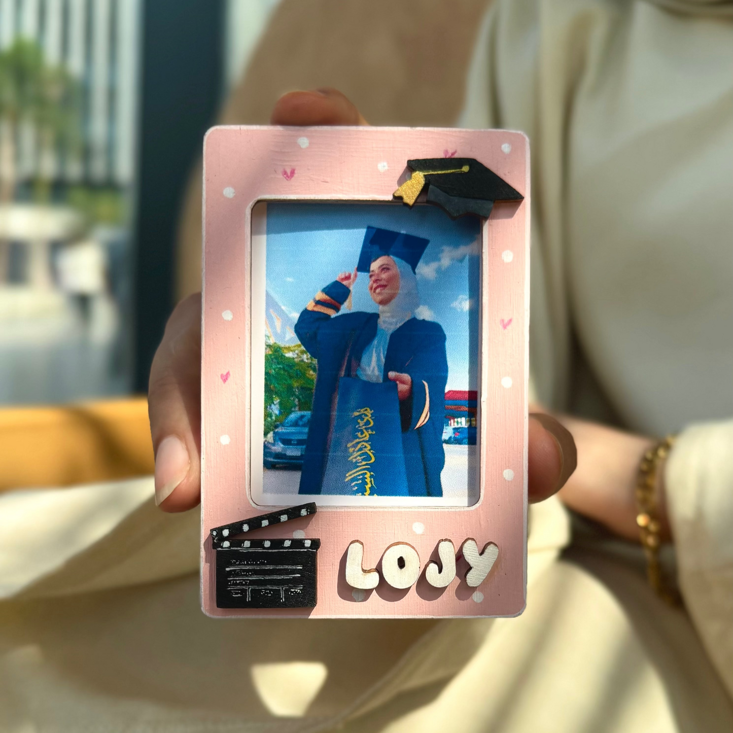 Person holding a pink photo frame with a picture of a person in a graduation gown.