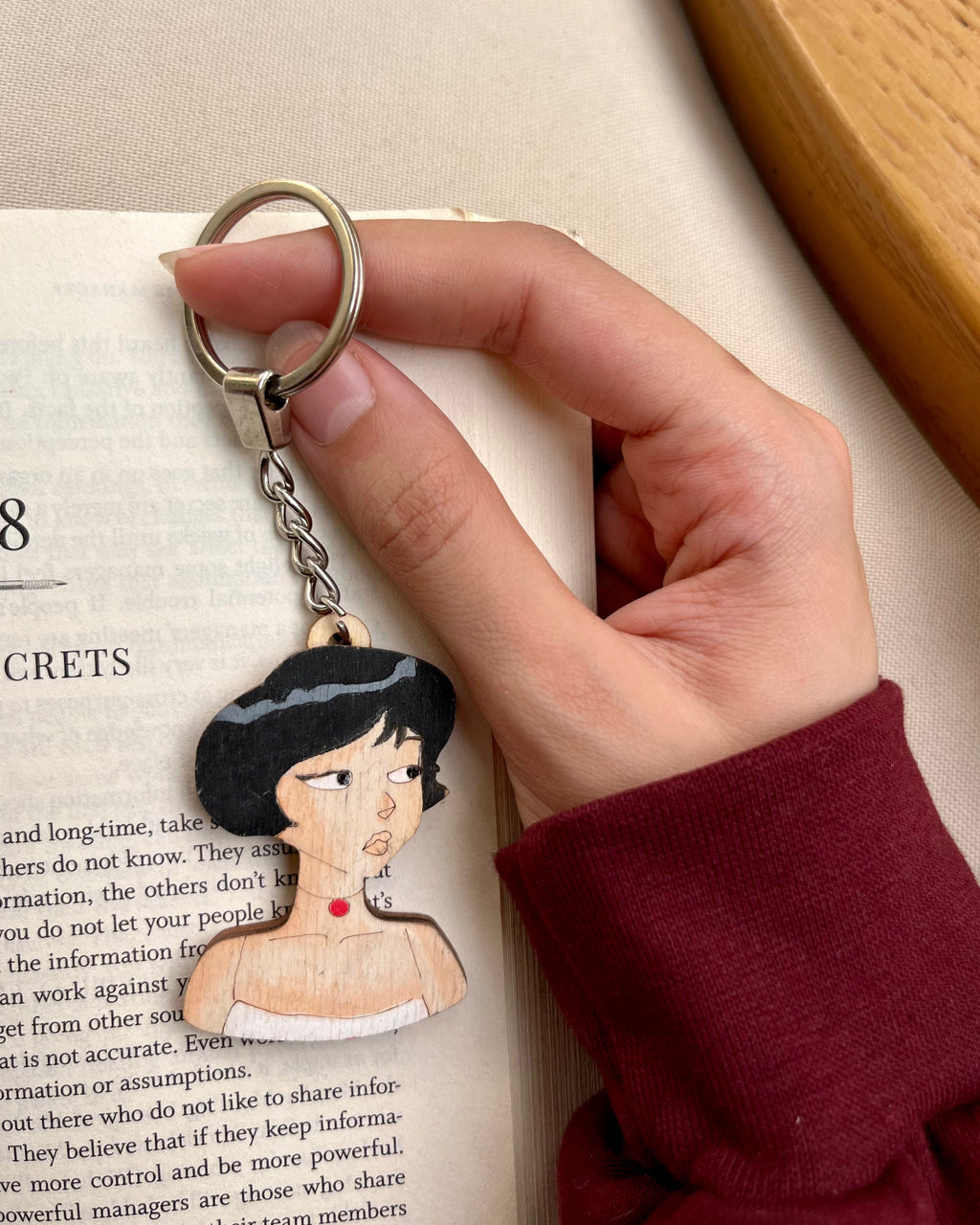 Keychain with an illustration of a woman held by a hand over an open book.