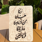 Decorative stone plaque with Arabic text on a wooden surface with plants in the background