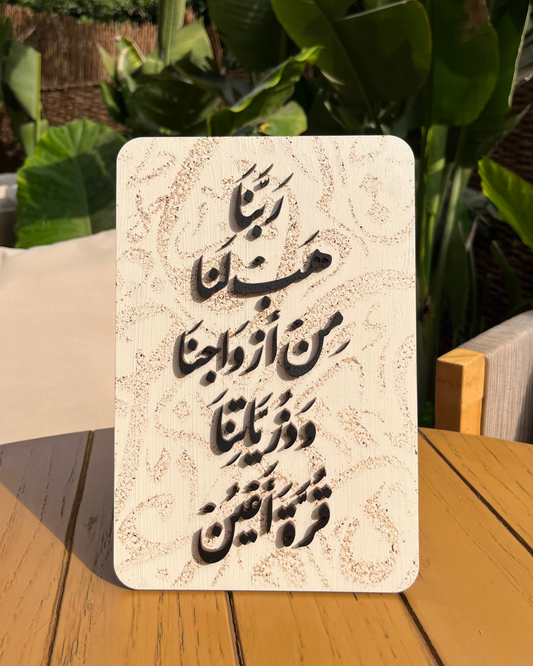 Decorative stone plaque with Arabic text on a wooden surface with plants in the background