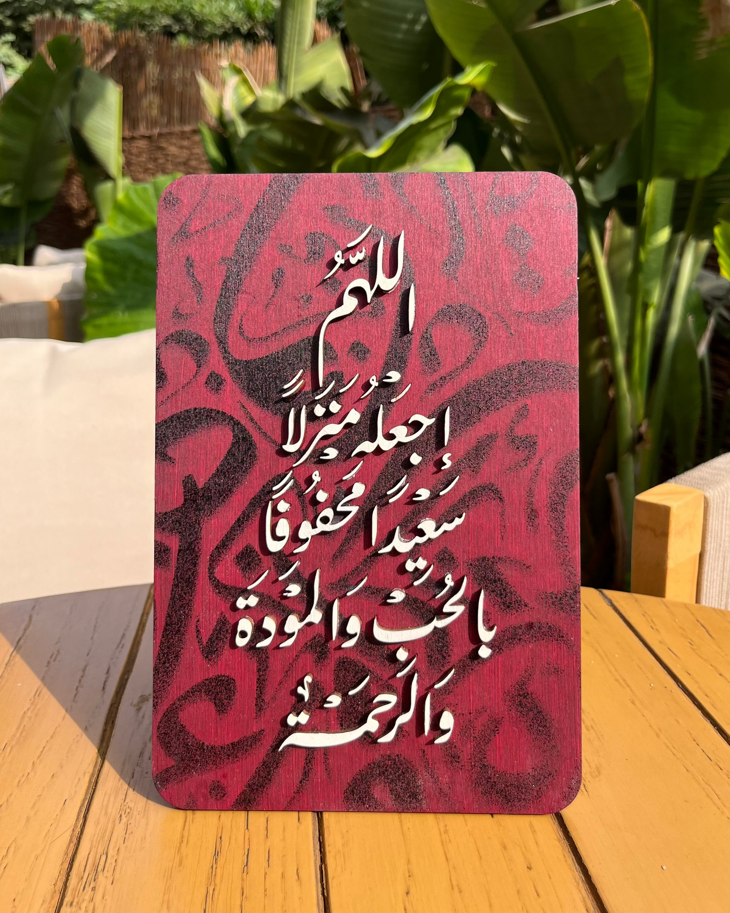Red notebook with Arabic text on a wooden surface with green plants in the background