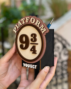 Hand holding a wooden bookmark with 'Platform 9 3/4' design and 'Yousef' engraving.