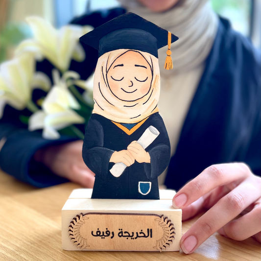 Graduation-themed figurine with a person wearing a hijab, held by a smiling person.